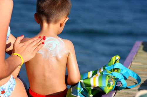 Mom applying sunscreen to son at beach
