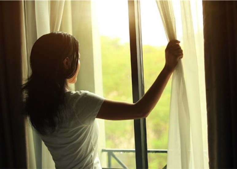 Woman pulling back curtains to look at sunrise