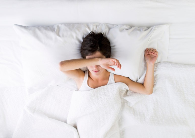 Woman in bed with her arm over her eyes
