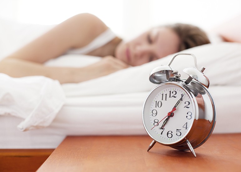 Woman sleeping with alarm clock on nightstand