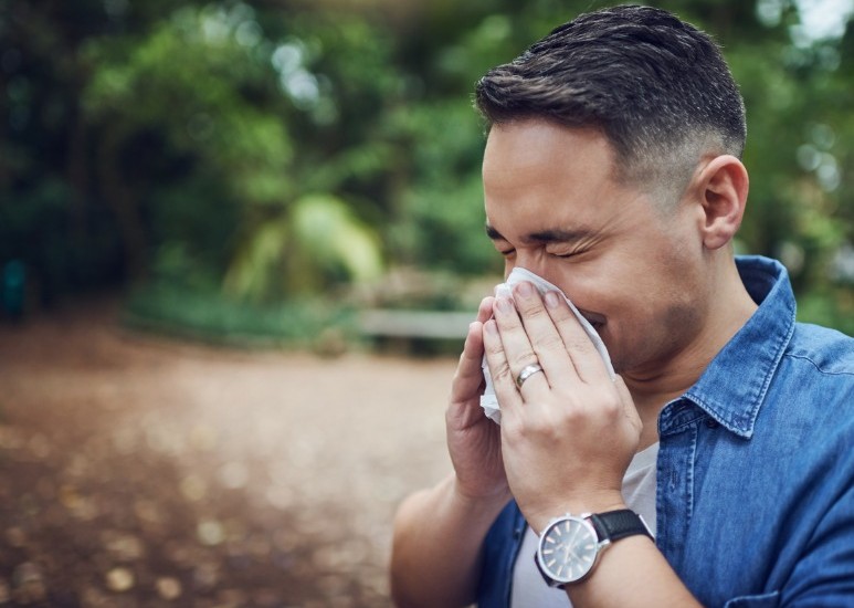 man sneezing while outdoors from allergies