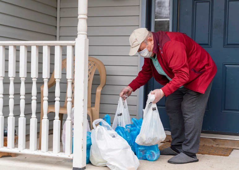 man putting groceries on porch for elderly