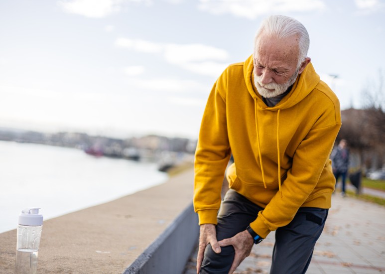 Active senior man experiencing knee pain while exercising outdoors.