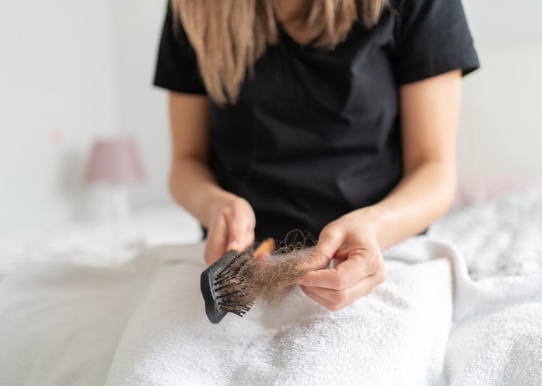 A woman notices a lot of hair in her hand when cleaning out her brush.
