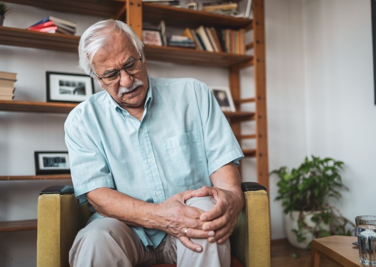  Man sitting in the living room holding his knee in pain