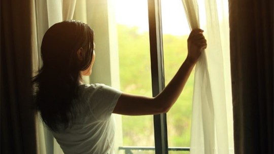 Woman pulling back curtains to look at sunrise