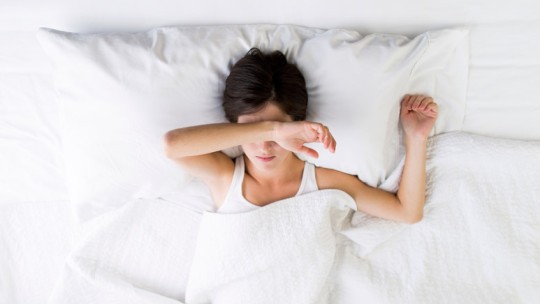 Woman in bed with her arm over her eyes