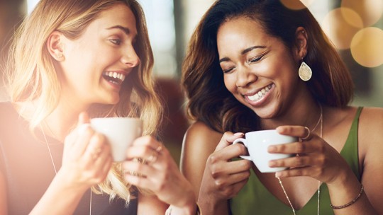 Two female friends laughing over coffee