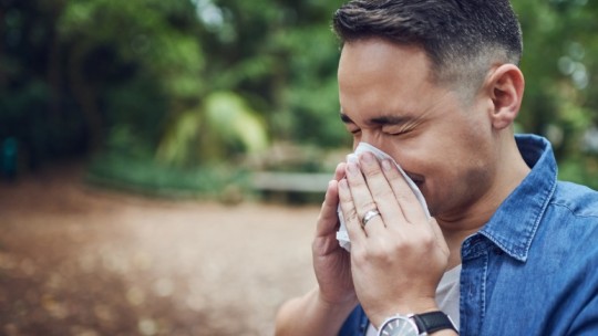 man sneezing while outdoors from allergies