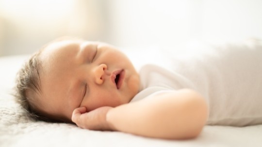 Baby sleeping in crib on flat fitted sheet
