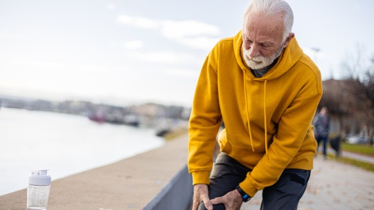 Active senior man experiencing knee pain while exercising outdoors.
