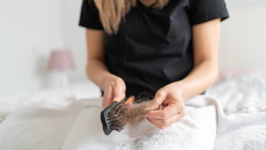 A woman notices a lot of hair in her hand when cleaning out her brush.