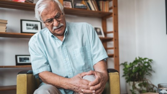  Man sitting in the living room holding his knee in pain