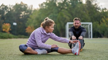 Woman and man stretching on athletic field